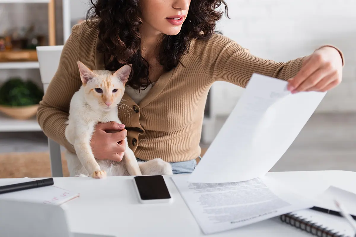 une femme avec son chat dans les bras relisant un contrat d'assurance